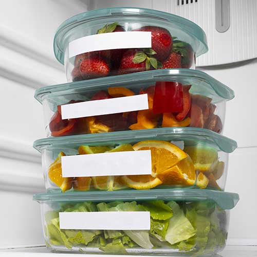 Boîtes de stockage alimentaire dans un réfrigérateur avec des fruits et légumes contenus dedans.